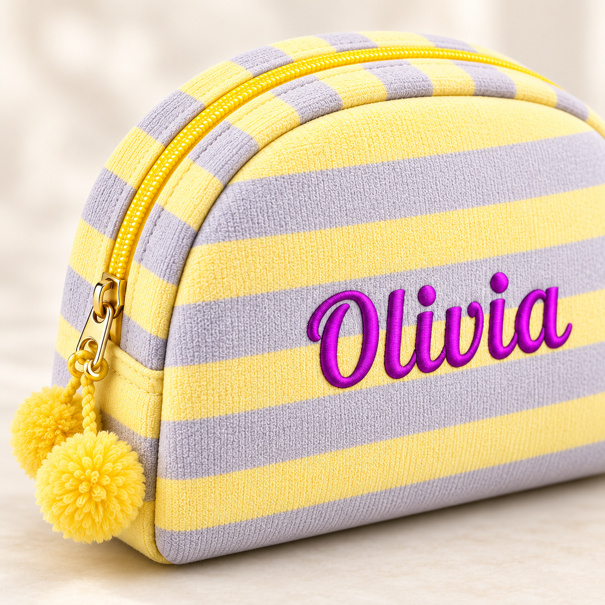 Close-up of embroidered name, striped fabric, curved zipper and yellow pom-poms.