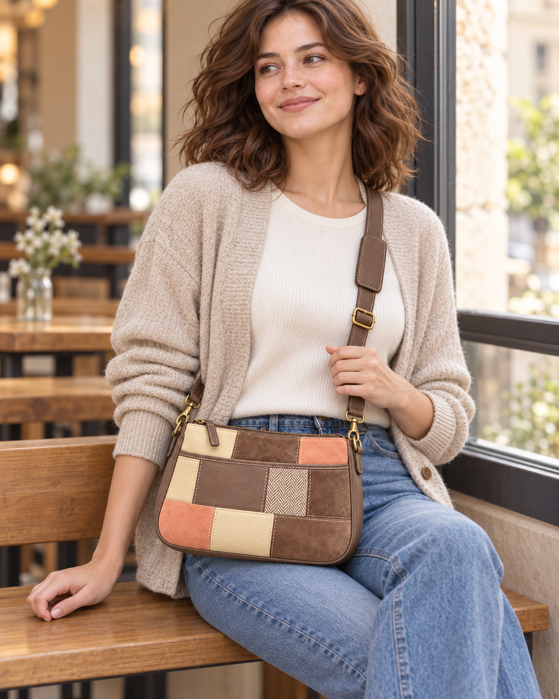 Woman seated by a cafe window wearing a taupe, apricot and cream patchwork crossbody bag.