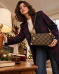 Young adult woman presenting the forest green and brown diamond-pattern shoulder bag, photographed from a low angle in a vintage Christmas living room.